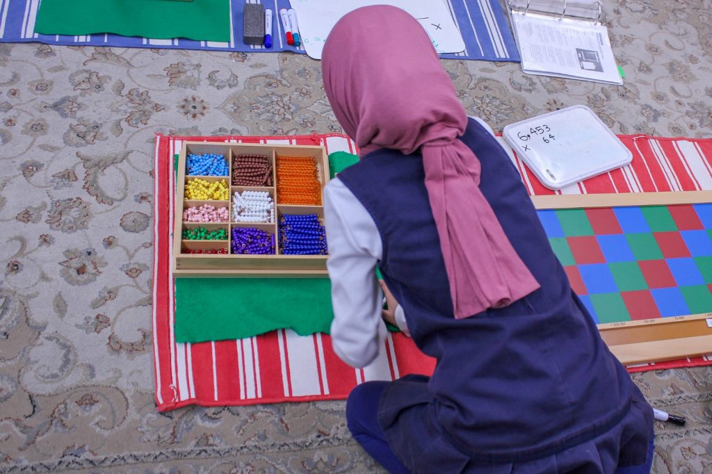 female student at Guide Academy sitting on the rug and using bead montessori material and checker board to solve math problems