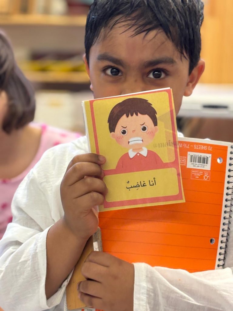 young boy holding a picture of a cartoon boy, picture says " I am angry" in arabic