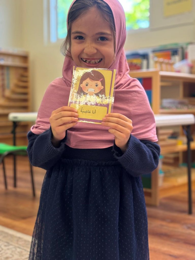 little girl wearing pink scarf holding a picture of a girl who is angry and it says " i am angry" in arabic
