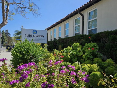 Front of Guide academy building green plants and poster that says Guide Academy